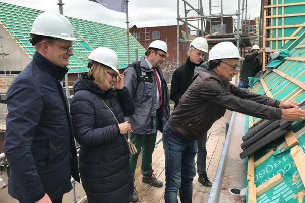 Verschillende mensen met een bouwhelm op staan op het dak en leggen dakpannen