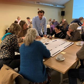 Bewoners zitten samen om tafel met een medewerker van Intermaris en plakken post-its op een poster