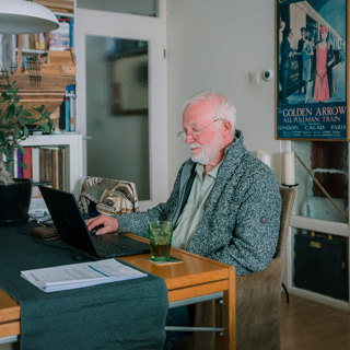 Oudere bewoner zit aan tafel achter de laptop