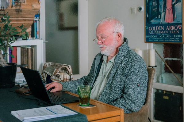 Oudere bewoner zit aan tafel achter de laptop