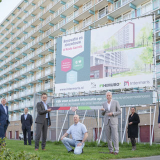 Diverse mensen staan bij het bouwbord voor een woongebouw