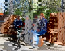 Vier bewoners zitten op een houten bankje voor een woongebouw