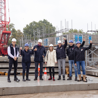 Groep mensen staat met een bouwhelm op op een betonnen plaat op de bouwplaats