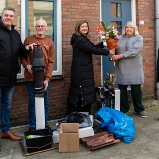 Bewoners staan met onderdelen van stadsverwarming voor hun woning, directeur vastgoed Iphigenia Westphal van Intermaris overhandigt bloemen aan een bewoner