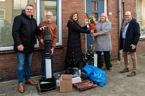 Bewoners staan met onderdelen van stadsverwarming voor hun woning, directeur vastgoed Iphigenia Westphal van Intermaris overhandigt bloemen aan een bewoner