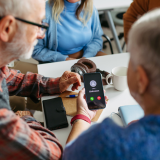 Personen zitten aan tafel met mobiele telefoon in de hand
