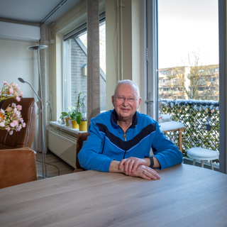 Bewoner met blauw jack aan zit aan tafel in zijn appartement