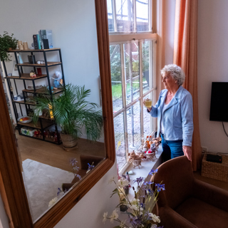 Vrouw heeft een kop thee vast en kijkt uit het raam naar werkzaamheden aan het woongebouw.
