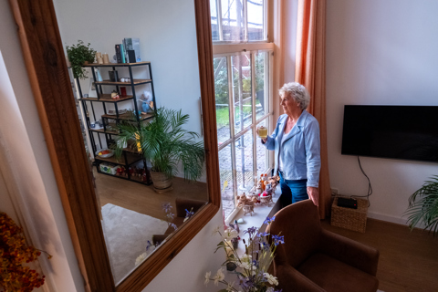 Vrouw heeft een kop thee vast en kijkt uit het raam naar werkzaamheden aan het woongebouw.
