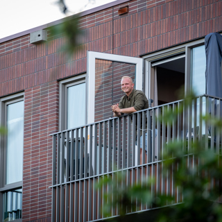 Bewoner staat op zijn balkon naar buiten te kijken